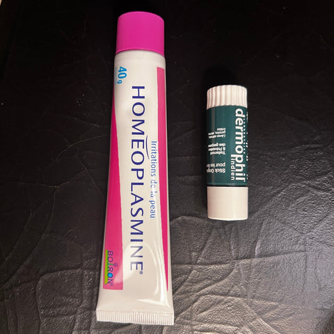 Two French products, a tube of Homeoplasmine and a stick of Dermophil, on a textured surface.