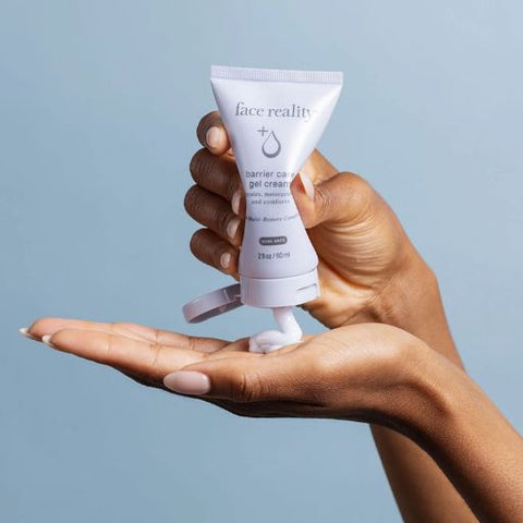 Hand holding a tube of 'face reality' gel cream against a light blue background