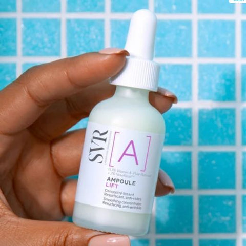 A hand holding a frosted glass dropper bottle of SVR Ampoule Lift serum against a blue tiled background.